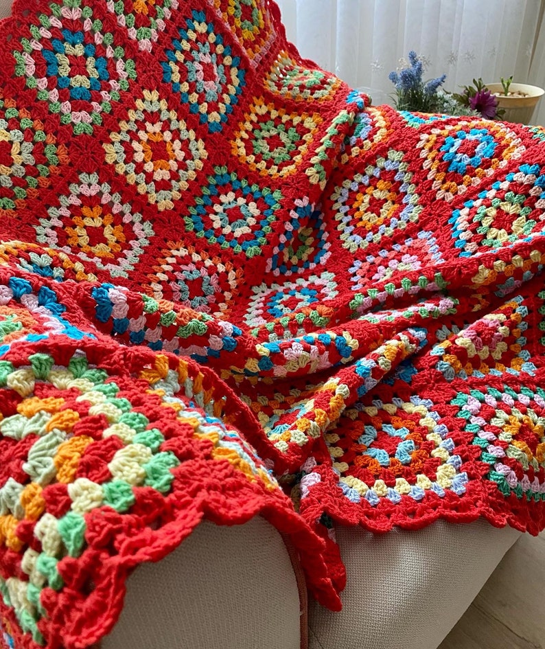 Peut inclure: Une couverture en crochet rouge avec un motif de carr&eacute;s de grand-m&egrave;re color&eacute;s. La couverture est faite de plusieurs couleurs, dont le rouge, l'orange, le jaune, le vert, le bleu et le rose.