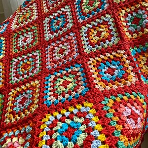 Peut inclure: Une couverture en crochet color&eacute;e avec un motif de carr&eacute;s de grand-m&egrave;re dans des tons de rouge, orange, jaune, vert, bleu et rose.