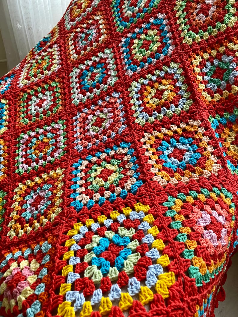 Peut inclure: Une couverture en crochet color&eacute;e avec un motif de carr&eacute;s de grand-m&egrave;re dans des tons de rouge, orange, jaune, vert, bleu et rose.