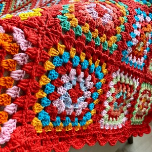 Peut inclure: Une couverture en crochet color&eacute;e avec un bord festonn&eacute;. La couverture est faite de plusieurs couleurs, dont le rouge, l'orange, le jaune, le vert, le bleu et le rose.