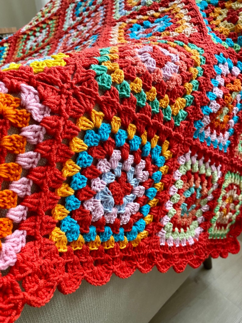 Peut inclure: Une couverture en crochet color&eacute;e avec un bord festonn&eacute;. La couverture est faite de plusieurs couleurs, dont le rouge, l'orange, le jaune, le vert, le bleu et le rose.