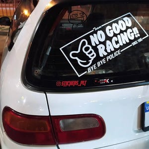 May include: White car with a rear window sticker saying "NO GOOD RACING!!" with a thumbs-up graphic. The sticker also includes the text "BYE BYE POLICE" and "SINCE 1985". A smaller sticker below says "@STICKERS_PLT".