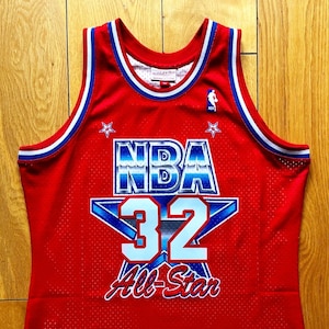 Puede incluir: Camiseta de baloncesto roja con ribetes azules y blancos. La camiseta tiene una gran estrella blanca con el número 32 en su interior y el texto "NBA All-Star" debajo.
