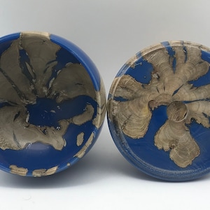 May include: A two-part wooden bowl set. The bowls are blue with natural wood grain patterns. The wood grain is a light tan colour, and the blue is a solid, deep colour. The bowl set is likely handmade and unique.
