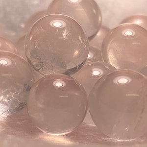May include: A group of clear, translucent, rose quartz spheres. The spheres are smooth and polished, and they have a slight pink hue.