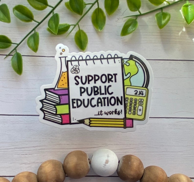Puede incluir: Una pegatina blanca con fondo amarillo y el texto "Apoya la educaci&oacute;n p&uacute;blica... &iexcl;funciona!" La pegatina presenta una pila de libros, un l&aacute;piz, una probeta, un globo terr&aacute;queo y una calculadora.