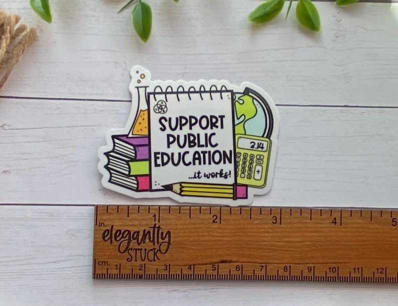Puede incluir: Una pegatina blanca con una ilustraci&oacute;n colorida de un cuaderno, una calculadora, un globo terr&aacute;queo, un l&aacute;piz y una pila de libros. El cuaderno dice "Apoya la educaci&oacute;n p&uacute;blica... &iexcl;funciona!"