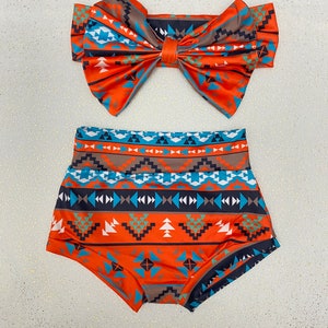 Puede incluir: Un conjunto de dos piezas que consta de una parte inferior de talle alto y una diadema a juego con un lazo grande. Ambos art&iacute;culos presentan un patr&oacute;n geom&eacute;trico vibrante en tonos naranja, turquesa, azul oscuro, blanco y marr&oacute;n en bandas.