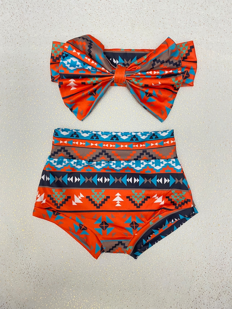 Puede incluir: Un conjunto de dos piezas que consta de una parte inferior de talle alto y una diadema a juego con un lazo grande. Ambos art&iacute;culos presentan un patr&oacute;n geom&eacute;trico vibrante en tonos naranja, turquesa, azul oscuro, blanco y marr&oacute;n en bandas.