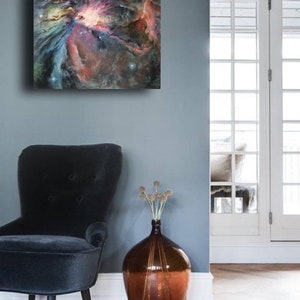 May include: A painting of a nebula in shades of pink, blue, and purple, hanging on a gray wall above a black armchair and a brown vase with dried flowers.