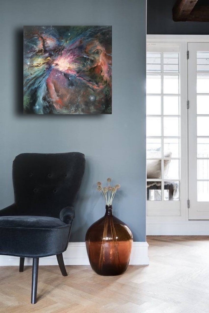 May include: A painting of a nebula in shades of pink, blue, and purple, hanging on a gray wall above a black armchair and a brown vase with dried flowers.