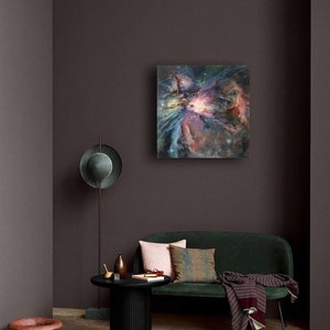 May include: A green velvet sofa with a throw blanket and pillows in a living room setting. A painting of a colorful nebula hangs on the wall above the sofa. A black side table with a vase and a book sits in front of the sofa.