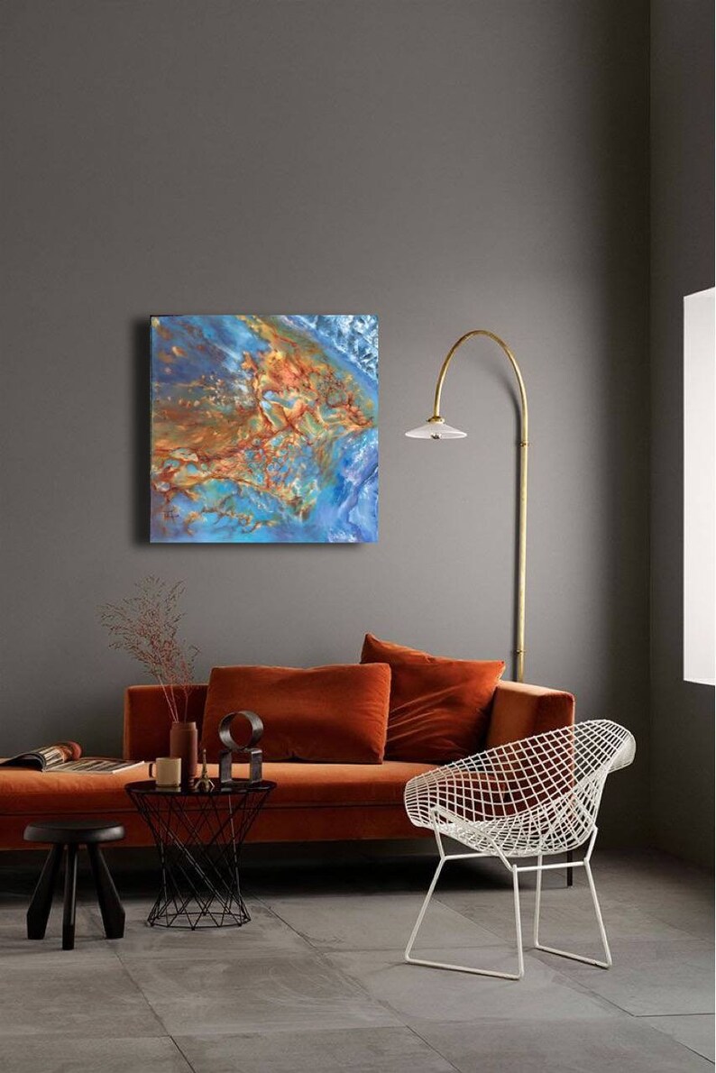 May include: Abstract painting with blue, orange, and brown colors. The painting is hanging on a gray wall above a burnt orange sofa and a white wire chair.