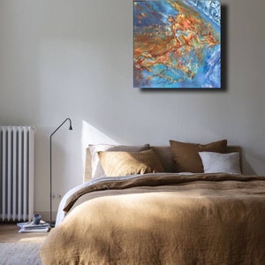 May include: Abstract painting with blue, brown, and gold colors. The painting is hanging on a wall above a bed with brown linen bedding.