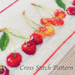 May include: A cross-stitch pattern featuring a cluster of cherries. The cherries are rendered in shades of red and orange, with green leaves and stems. The words "Cross Stitch Pattern" are at the bottom.