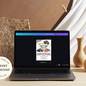 May include: A laptop displays a birthday invitation template with monster truck graphics. The invitation features a checkered flag design and the text "MICHAEL 2ND JAM". The laptop is on a light brown surface, with decorative vases and a stone block in the background.