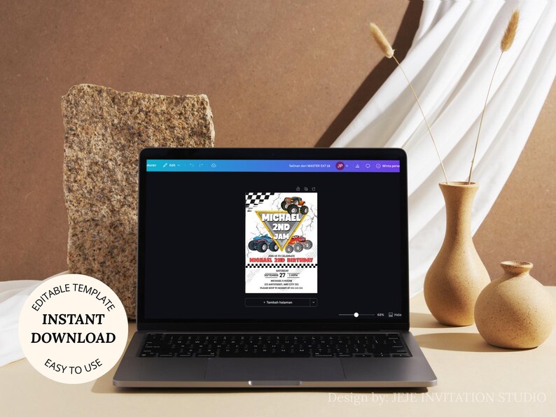 May include: A laptop displays a birthday invitation template with monster truck graphics. The invitation features a checkered flag design and the text "MICHAEL 2ND JAM". The laptop is on a light brown surface, with decorative vases and a stone block in the background.