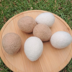 May include: Six wool dryer balls, three white and three brown, on a wooden surface.