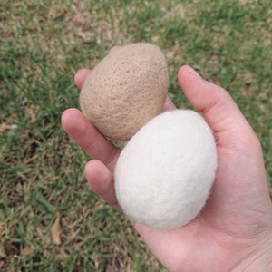 May include: Two wool dryer balls, one beige and one white, in a hand.