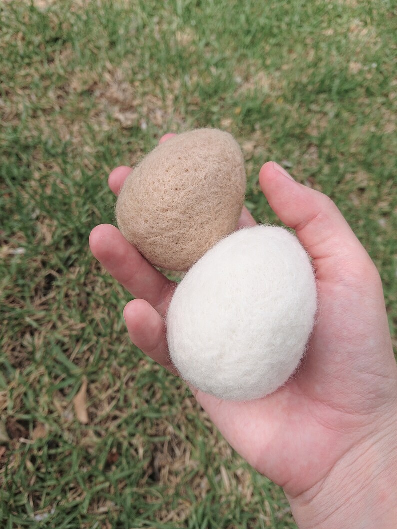 May include: Two wool dryer balls, one beige and one white, in a hand.