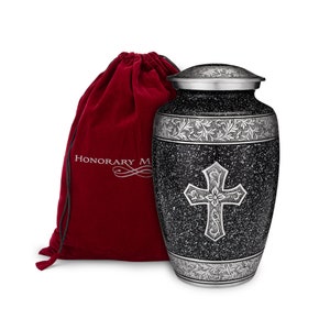 May include: A black and silver cremation urn with a cross design and a silver floral border. The urn comes with a red velvet bag. "Honory Memorials" is printed on the bag.