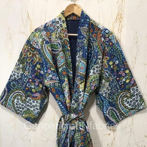 Könnte beinhalten: Ein langärmeliger Morgenmantel mit einer leuchtend blauen Grundfarbe und einem mehrfarbigen Paisley- und Blumenmuster. Das Kleidungsstück verfügt über einen passenden Bindegürtel, weite Ärmel und ein dunkelblaues Innenfutter am Kragen.