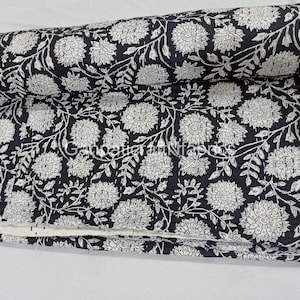 May include: A rolled-up, black and white floral quilt. The quilt features a repeating pattern of large, white flowers and leaves against a black background. The edges are neatly finished, and the quilt appears soft and comfortable.
