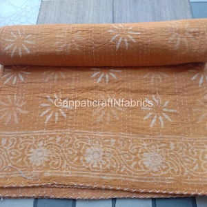 May include: A mustard yellow cotton quilt featuring a repeating white sunburst pattern and a floral border design. The fabric has visible white running stitch details throughout and the text GanpaticraftNfabrics is printed across the center.