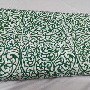 May include: A white and green patterned quilt. The quilt features a repeating design of green, swirling, floral-like shapes against a white background. The edges are stitched with green thread. This bedding item is suitable for a bed or as a decorative throw.