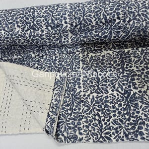May include: A rolled-up, white and navy blue floral patterned quilt. The quilt is partially unrolled, revealing a section with visible stitching. The floral design is repeated across the entire quilt. The text "Ganpaw" is visible on the quilt.