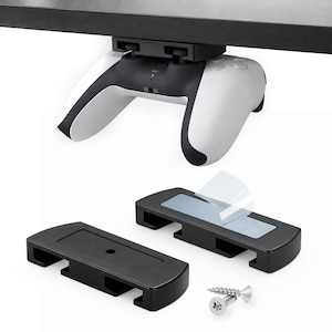Peut inclure: Une manette de jeu blanche et noire est fixée sous une surface sombre. Deux supports de montage noirs avec des coussinets adhésifs et des vis sont présentés, suggérant un système de fixation pour la manette.