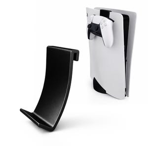 Op de afbeelding: Een zwarte console standaard en een wit en zwarte game console met een witte controller. De standaard heeft een gebogen, haakvormig ontwerp. De game console is wit met zwarte accenten, en de controller is wit met zwarte knoppen.