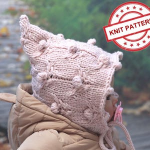 May include: A pink knitted baby hat with a pointed hood and bobbles. The hat is made with a textured stitch pattern. "Knit Pattern" is written on a red circle stamp.