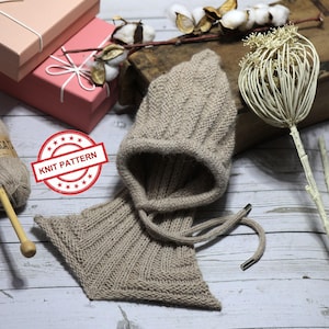 Könnte beinhalten: Ein gestricktes beiges Mützen- und Schal-Set mit passendem Design. Das Set wird mit einem Knäuel Alpaka-Garn, Stricknadeln und zwei rosa Geschenkboxen präsentiert. Ein Stempel lautet "KNIT PATTERN".