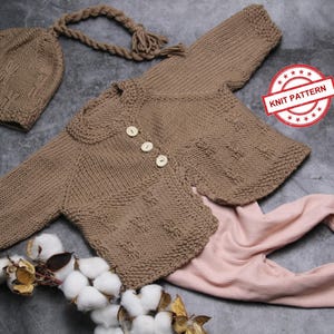 May include: A brown knitted baby cardigan with button closures, a matching brown knitted hat, and a pair of pink knitted pants. The image includes the text "KNIT PATTERN".