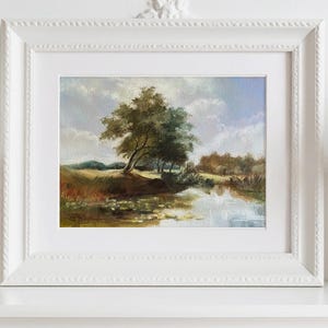 Landscape artwork with river and blue sky in ornate white frame in a classic light interior