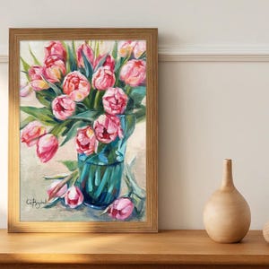 A framed artwork featuring pink tulips in a green vase against light cream backdrop