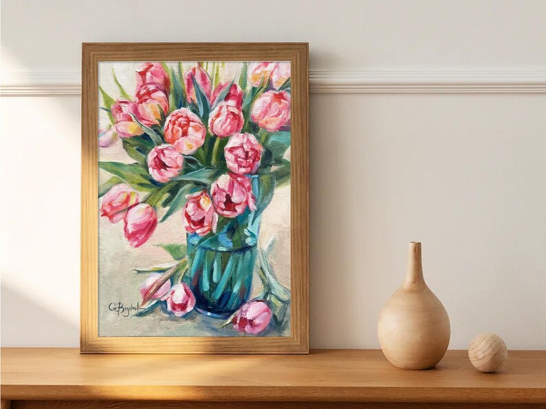 A framed artwork featuring pink tulips in a green vase against light cream backdrop
