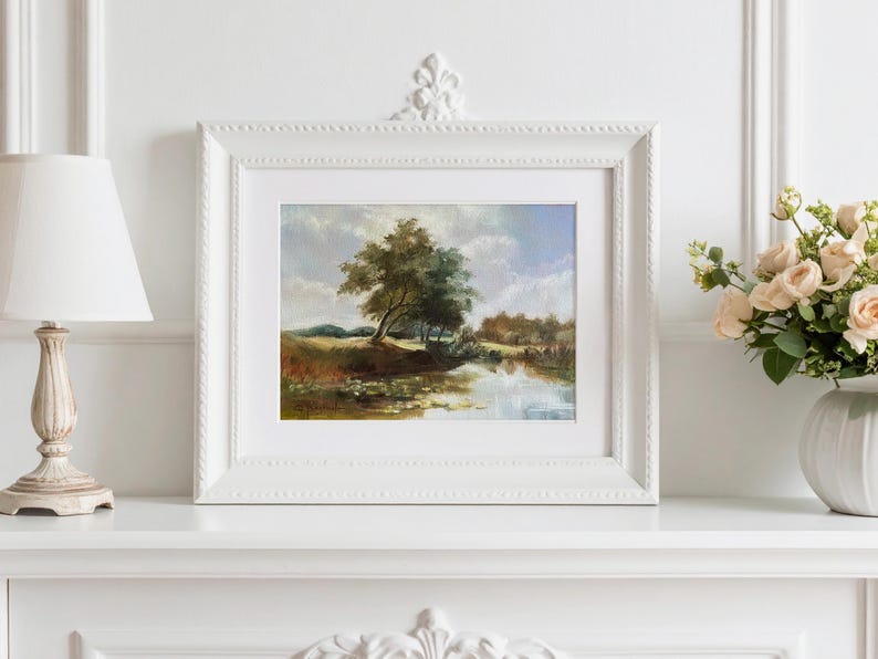 Landscape artwork with river and blue sky in ornate white frame in a classic light interior