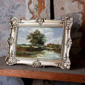 French landscape print in ornate frame displayed on a shelf, river scene with trees and sky, elegant classic wall decor for any room