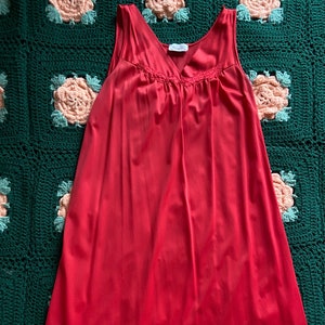 Könnte beinhalten: Ein rotes, ärmelloses Nachthemd mit einer Spitzenborte am Ausschnitt. Das Nachthemd hat einen gerafften Oberteil und einen geraden Rock.