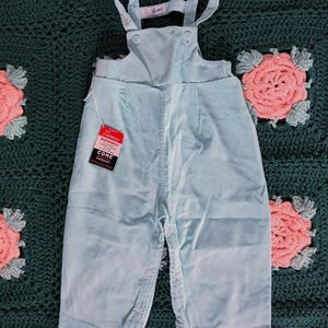 May include: Light blue corduroy overalls with adjustable straps and a button closure. The overalls have a tag that reads "Thomas Washable Cone Corduroy."
