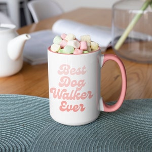 May include: White ceramic mug with a pink rim and handle. The mug has the text "Best Dog Walker Ever" in pink script. The mug is filled with pastel-colored marshmallows.