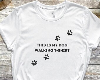 以下が含まれることがあります： 「This is my dog walking t-shirt」という文字と4つの足跡がプリントされた白いTシャツです。