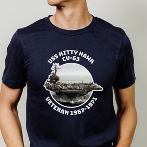May include: A navy blue t-shirt with a white graphic of the USS Kitty Hawk CV-63 aircraft carrier. The graphic includes the text "USS Kitty Hawk CV-63 Veteran 1967-1971".