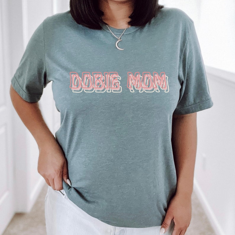 May include: A teal blue t-shirt with the text "DOBIE MOM" in pink and white outlined letters.