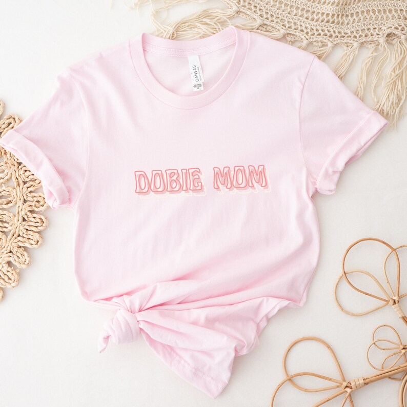 May include: Pink t-shirt with the text "DOBIE MOM" in a pink and orange outline.