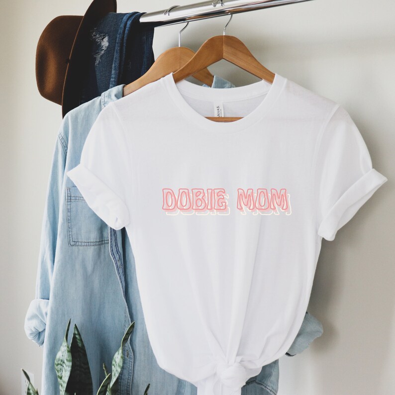 May include: White t-shirt with the text "DOBIE MOM" in pink outlined letters.