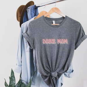 May include: Gray t-shirt with the text "DOBIE MOM" in pink outlined letters.