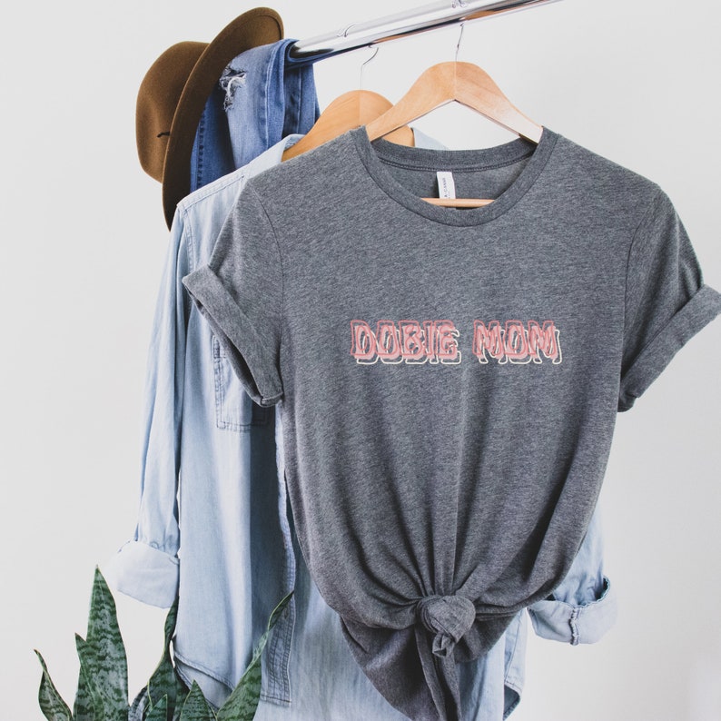 May include: Gray t-shirt with the text "DOBIE MOM" in pink outlined letters.